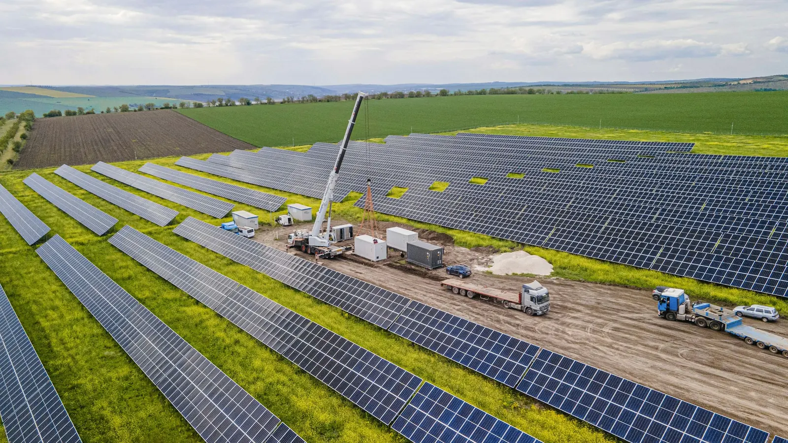 Vista aérea de una planta solar en construcción, con una grúa entre las filas de paneles